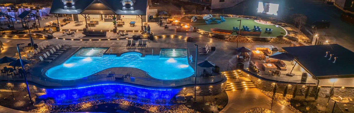 Resort pool lit blue at night, with stone walls, a fire pit lawn and string lights, built by Teaster's Natural Creations